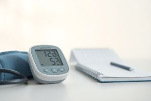 Digital blood pressure monitor and calendar planner on a table, representing regular health tracking.