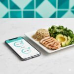 Smartphone macro tracking app next to balanced meal with chicken, quinoa, and avocado